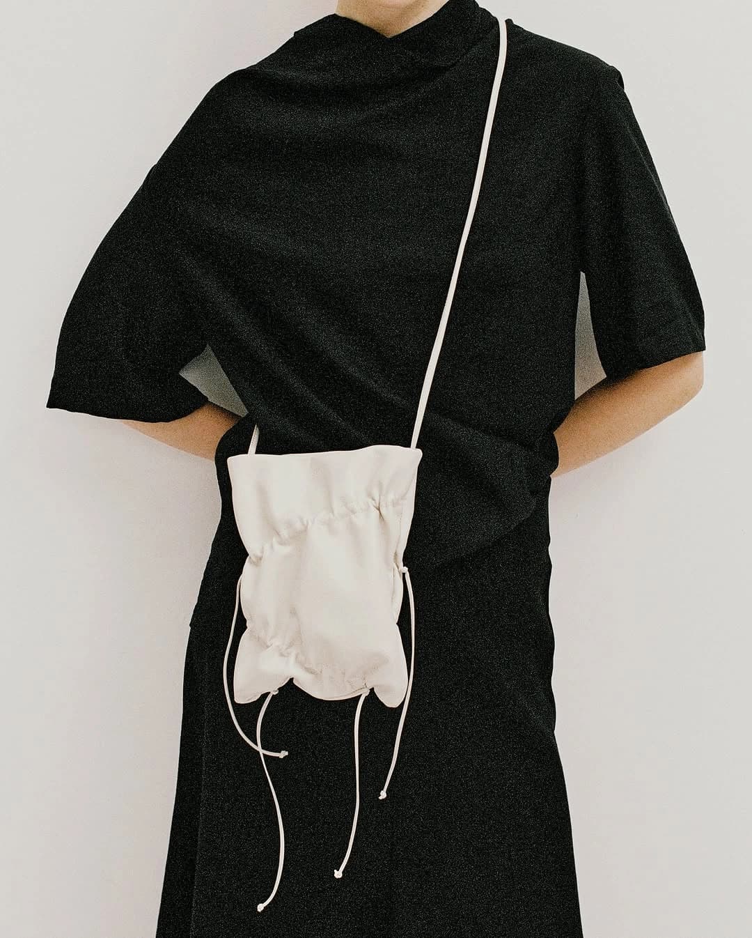 An all-black draped outfit with a soft leather tote, shot in a bright studio