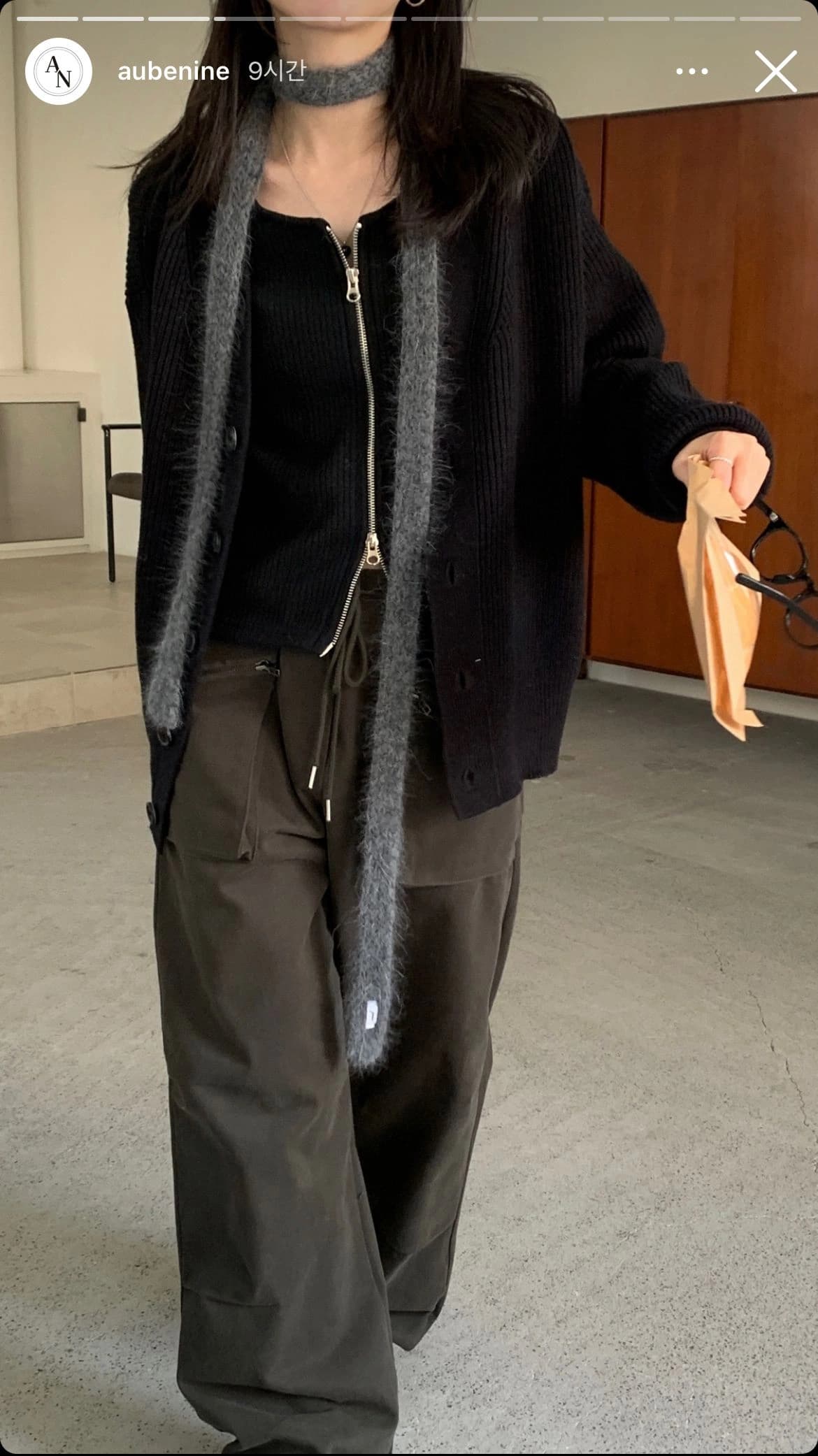 A phone snapshot of a full-length fit — black knit cardigan over olive trousers