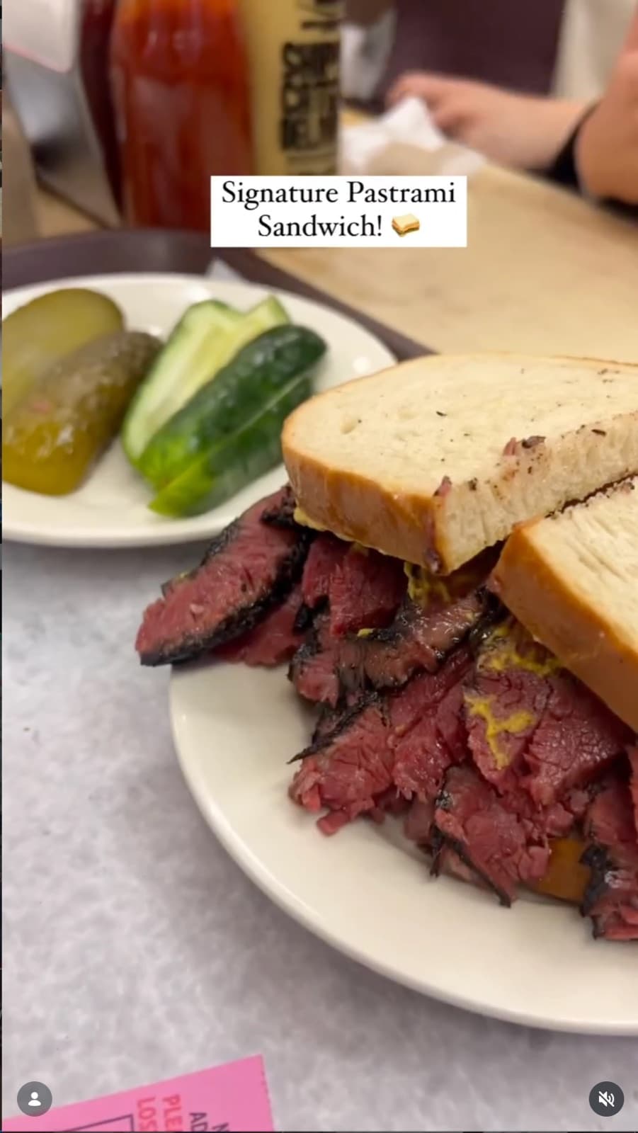 A towering pastrami sandwich at Katz's Deli with a plate of pickles behind it