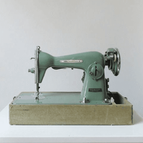 A vintage sea-green sewing machine on a worn wooden base