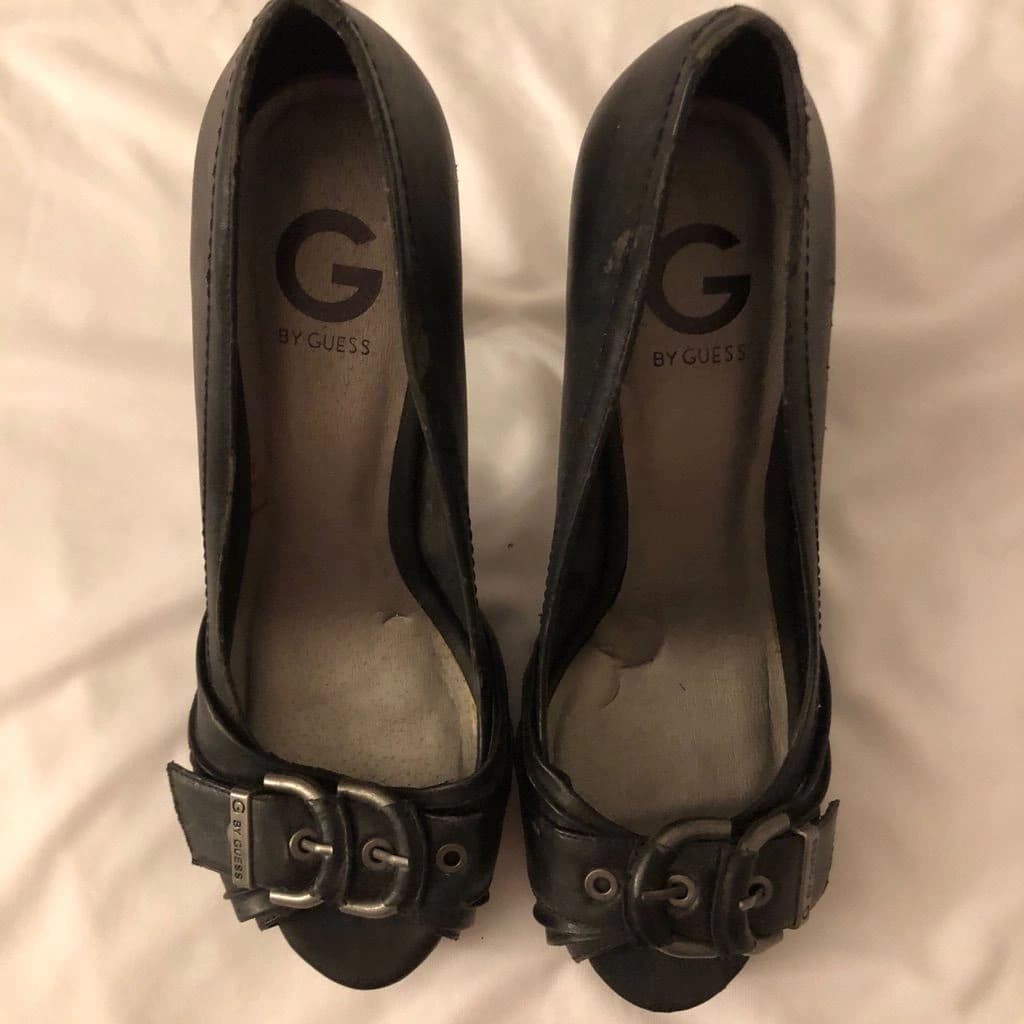 A pair of black buckled peep-toe heels on a white sheet